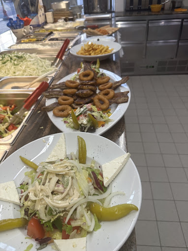 Blick entlang der Speisenausgabe — Salatteller mit Schafskäse vorn, Calamaris-Ringe auf Salat, Pommes-Schale im Hintergrund